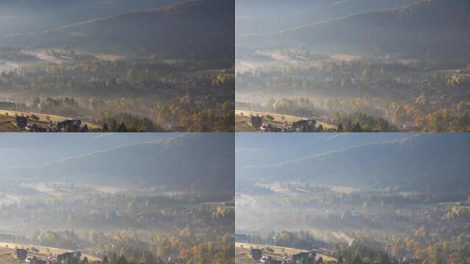 美丽的雾拂晓山谷高山村庄在时间的推移拍摄。建筑物和树木被滚滚的云雾覆盖。温暖的初升的太阳照亮了薄雾中