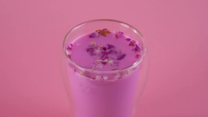 粉色月亮牛奶。玫瑰花瓣在玻璃杯中旋转。一杯玫瑰牛奶