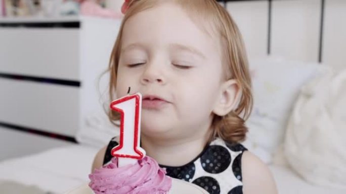 一个快乐可爱的1岁女孩的生日聚会，并在蛋糕上吹蜡烛。