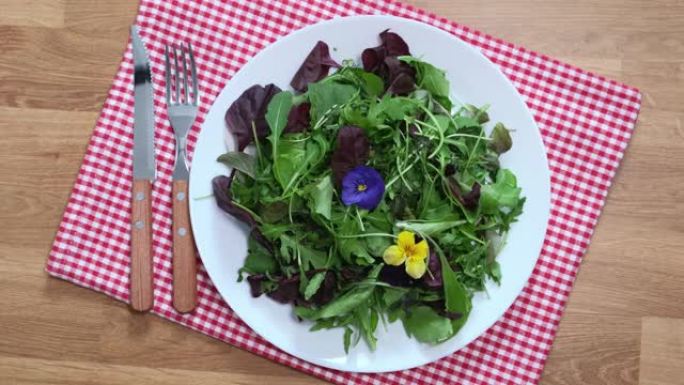 新鲜沙拉盘，混合绿色莴苣叶和紫罗兰花。菜肴装饰，餐桌。准备在桌子上吃一份。健康食品绿色餐，酮或古饮食