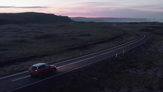 北欧景观中的公路旅行。跟踪夜间乡村道路上行驶的汽车。色彩丰富的天空。冰岛