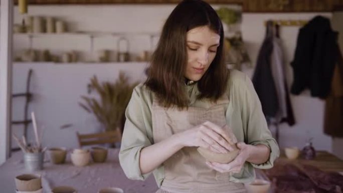 美丽的工匠在陶艺作坊里做粘土碗。她看着产品，微笑着。喜爱的爱好和创造性发展的概念