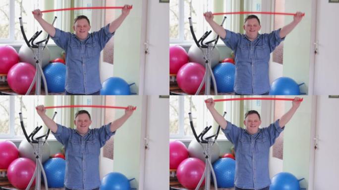 一个患有唐氏综合症的快乐残疾人对着镜头微笑正在进行体育锻炼，我将一根体操棒举到顶部。