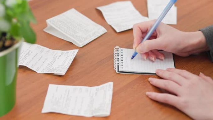 一个女人用薪水记账，把费用写在笔记本上。双手特写。商业和保险