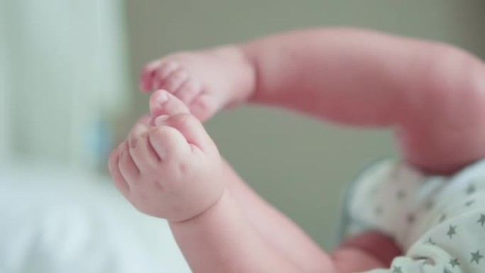 可爱的婴儿新生儿手的镜头伸到或玩耍，躺在床上时触摸脚。幸福的家庭，天真的小新婴儿在生命的第一天就很可