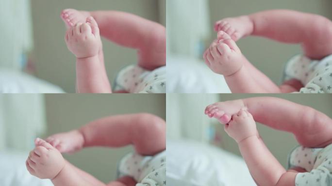 可爱的婴儿新生儿手的镜头伸到或玩耍，躺在床上时触摸脚。幸福的家庭，天真的小新婴儿在生命的第一天就很可