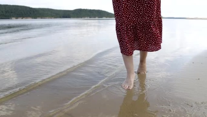 穿着红色连衣裙的女性腿沿着山湖的沙滩奔跑，与自然统一的概念