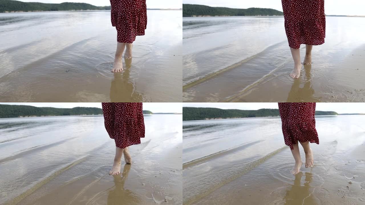 穿着红色连衣裙的女性腿沿着山湖的沙滩奔跑，与自然统一的概念