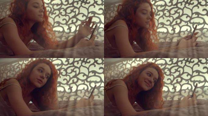 一头红头发的漂亮女人躺在床上，透过手机看