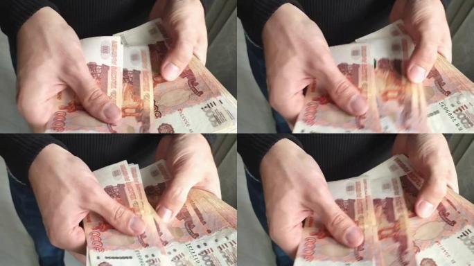 一个人手里拿着一大笔钱。一个男人的手的特写镜头数了一捆5,000俄罗斯卢布的钞票