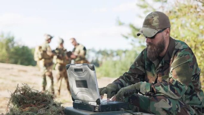 一群士兵穿着战袍，准备好装备和武器，在远处等待着坐在电脑前向基地发送数据的指挥官