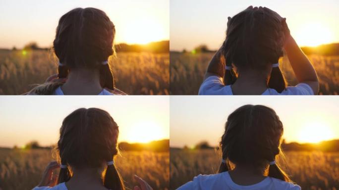 漂亮的女孩子站在草地上，拉直她的金发。可爱的小女孩在草地上看着美丽的晚霞。模糊美丽的背景。自由概念。