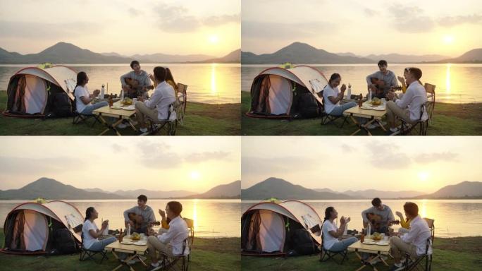亚洲四个年轻朋友在河边露营野餐，他们聊天，大笑，喝酒庆祝啤酒。休闲装，夏天的时候，夕阳的亮光。
