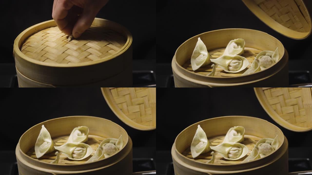 一个男人的手打开了展示中国饺子馄饨的竹蒸箱的盖子，在黑色背景上关闭。餐厅中餐。亚洲蒸汽食品点心，馅饺