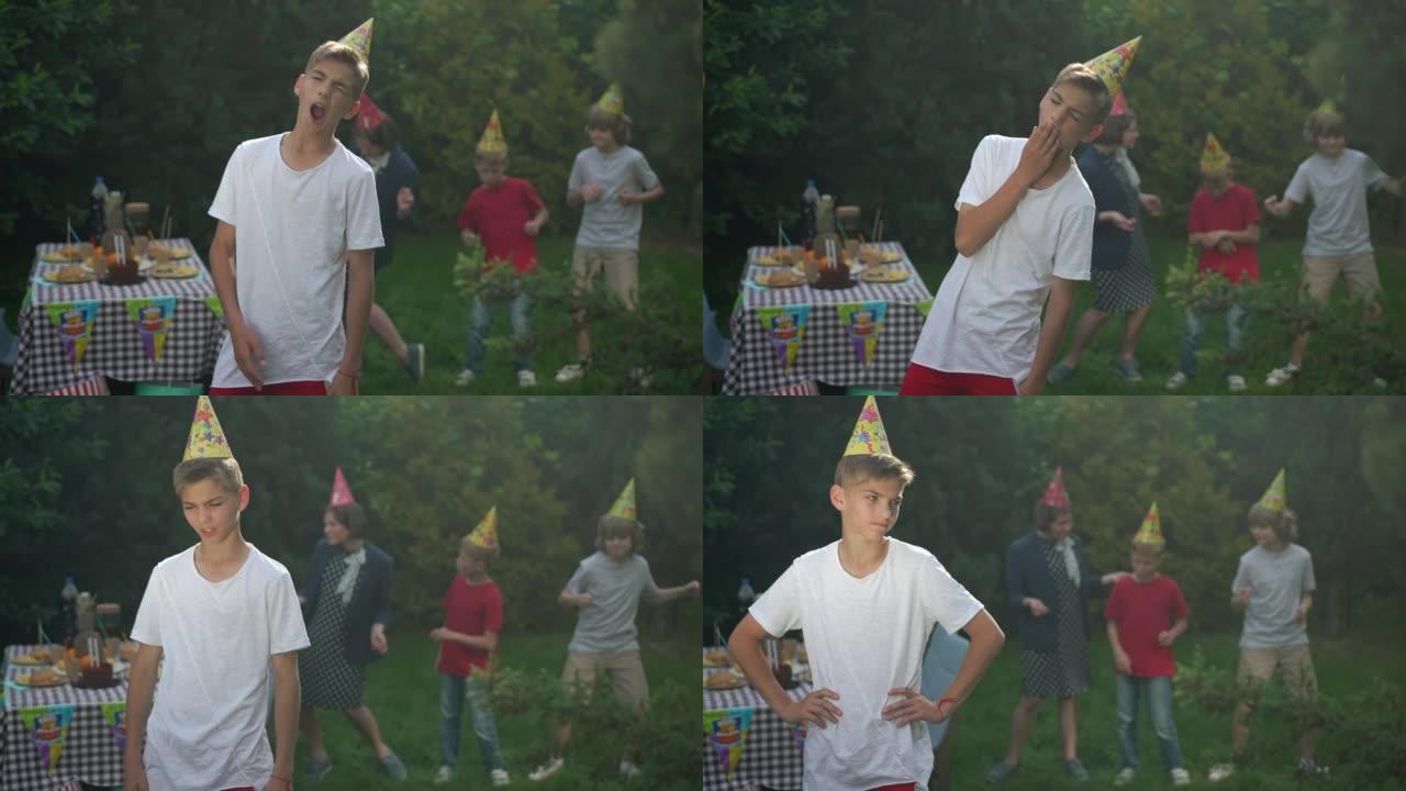 无聊的十几岁男孩在生日聚会上打哈欠的肖像，模糊的一群朋友在背景中跳舞。毫无兴趣的高加索少年在春夏公园