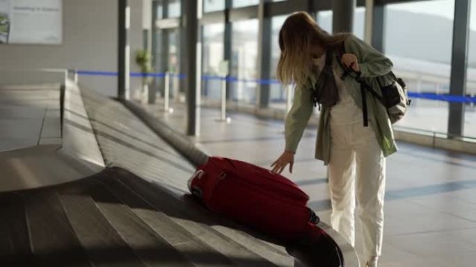 在机场等候行李旁边的旅行妇女，在传送带上检查箱子