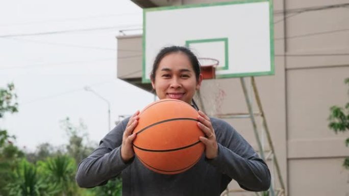 亚洲女子手持篮球在室外篮球操场上看着相机。