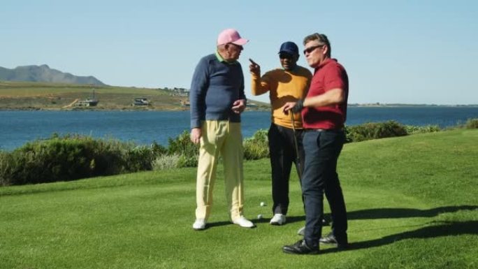 男性高尔夫球手在阳光明媚的湖边高尔夫球场球座上聊天