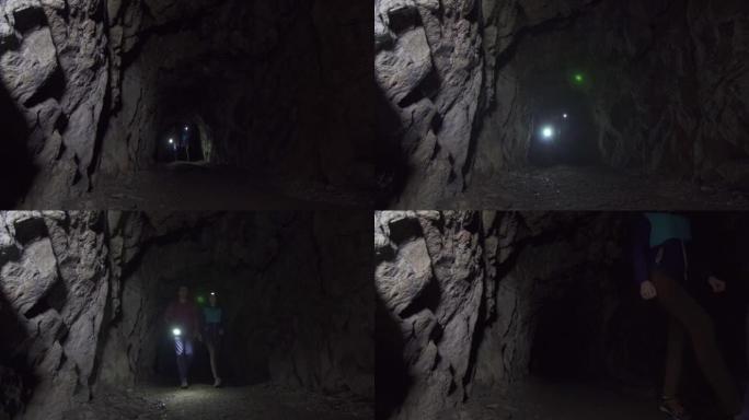 女孩和男人的游客用手电筒穿过一个黑暗的深洞
