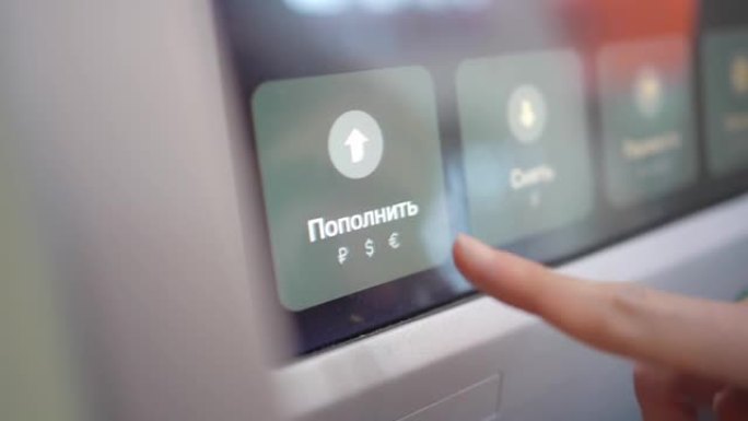 妇女的手将俄语的充值按钮放在atm屏幕上。