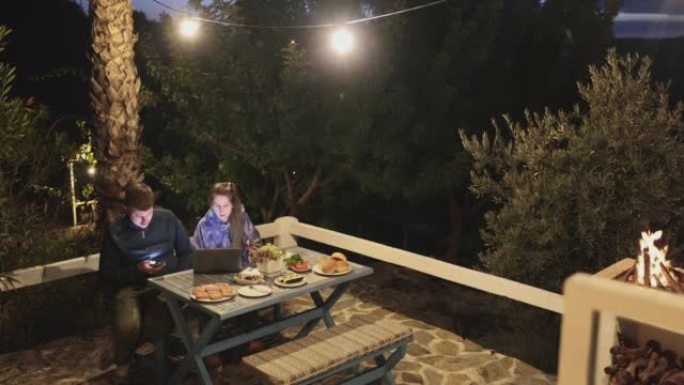 女人和男人享受汉堡烧烤野餐，并在家庭露台上用笔记本电脑工作