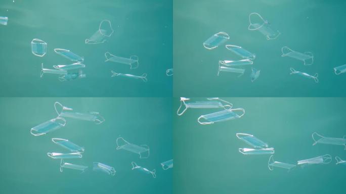 用过的医用口罩在蓝色水柱水下漂移。冠状病毒正在造成污染，因为废弃的口罩会污染海洋和塑料垃圾。特写，慢