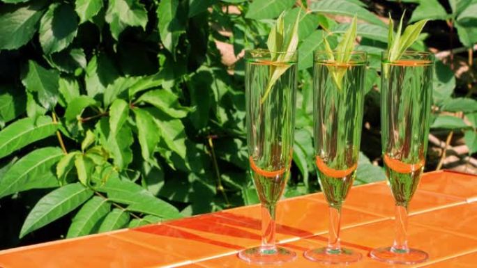 水晶眼镜中的清爽鸡尾酒，橙色瓷砖背景上绿叶，反射棕榈树。炎热夏日的天然冷饮。苏打水薄荷滋补品。热带派