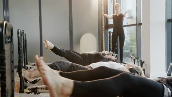 康复瑜伽课程一群不同年龄的人仰卧在年轻成功的专业教练的监督下进行腿部锻炼