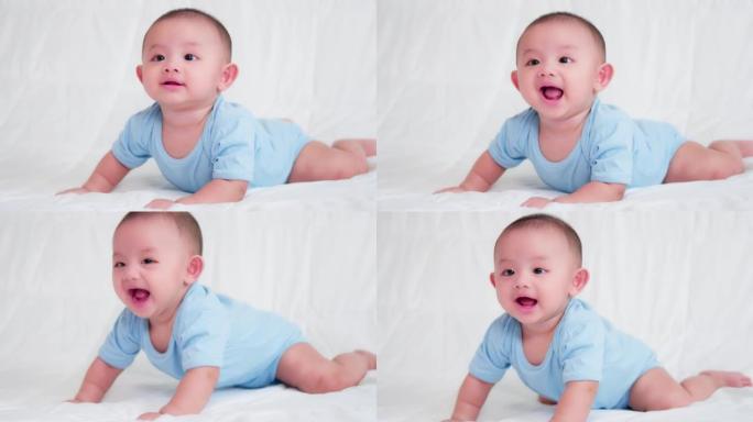 幸福的家庭，可爱的亚洲新生婴儿穿着蓝色衬衫躺着，在床上爬行玩耍，看着相机笑着笑脸。天真的小新婴儿可爱