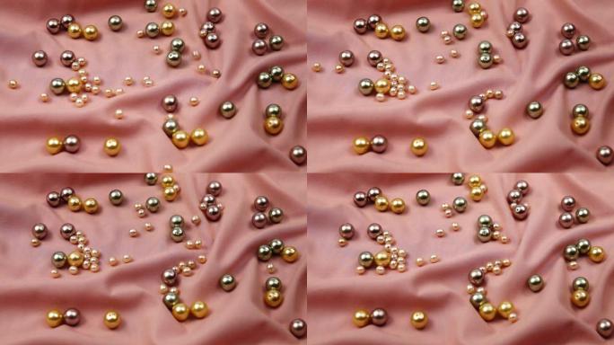 珍珠珠子不同颜色在桃色丝绸上滚动，背景，慢动作