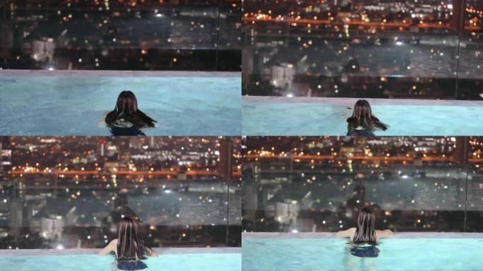 快乐的广角年轻女子在室外游泳池，晚上可以看到城市的景色