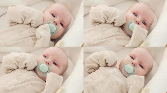 一个可爱的婴儿的特写镜头，嘴里叼着奶嘴，躺在白色毯子上，抽泣着