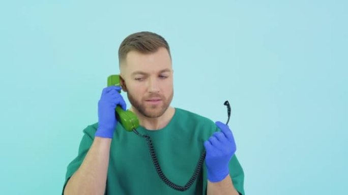 身穿绿色制服、戴着蓝色手套的医生惊讶地手里拿着一个旧手机