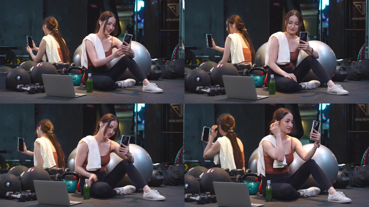一名亚洲妇女在健身房休息，正在使用毛巾擦干脸，并通过智能手机视频通话放松。