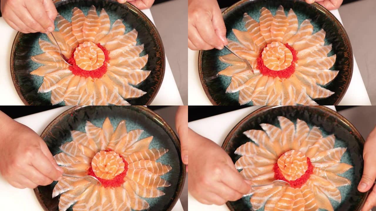 食物电镀-厨师用茶匙将红鱼子酱放在生鱼片鲑鱼玫瑰周围的圆形盘子上