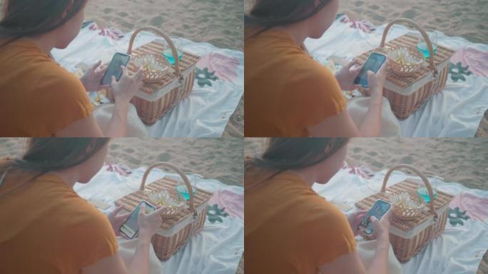 女人在海滩上的毯子上野餐时玩手机