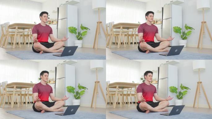 亚洲英俊活跃的年轻人在客厅地板上做瑜伽。穿着运动服的有魅力的男性花休闲时间在家中遵循笔记本电脑上的在