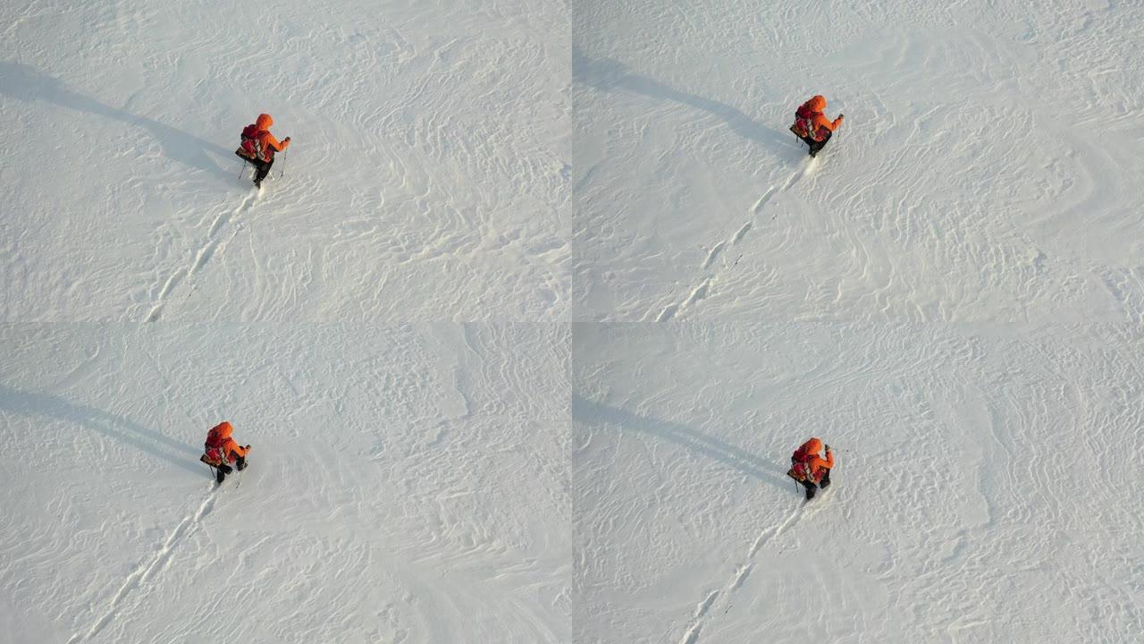 空中全高清镜头-一个背着背包和棍棒的人走过白雪皑皑的沙漠，留下一连串的脚印。在极冷条件下生存的概念