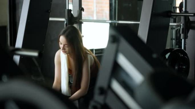 一名亚洲妇女在健身房休息，在健身时间用减肥机锻炼后，用毛巾擦干脸，喝蔬菜有机果汁