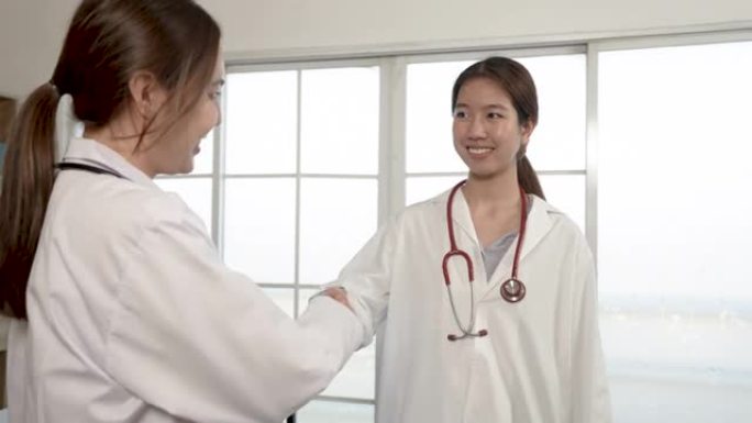 4k，两名身穿白衫的亚裔女医生手牵手。祝贺彼此通过两家医院的合作使活动取得成功。
