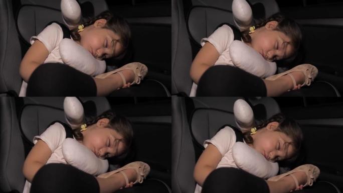 一个小女孩晚上睡在汽车座椅的后座上。汽车在路上。开车长途旅行后，孩子累了。不舒服的睡姿。自动睡觉枕头