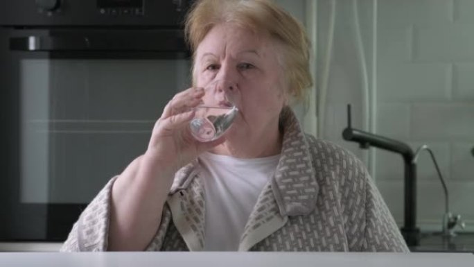 老年妇女在家中厨房用玻璃杯喝水