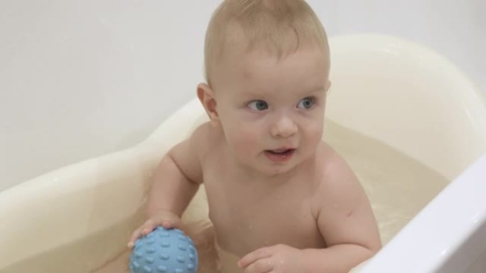 可爱的小孩洗澡和玩玩具，孩子玩洗澡玩具橡胶球，10个月大的男婴在干净的水中洗澡特写。儿童卫生和保健的