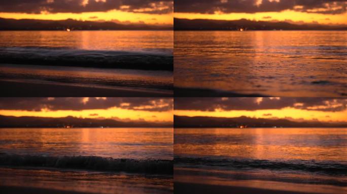 日落时沙子上平静的波浪特写。天空的金色和模糊背景中的山脉