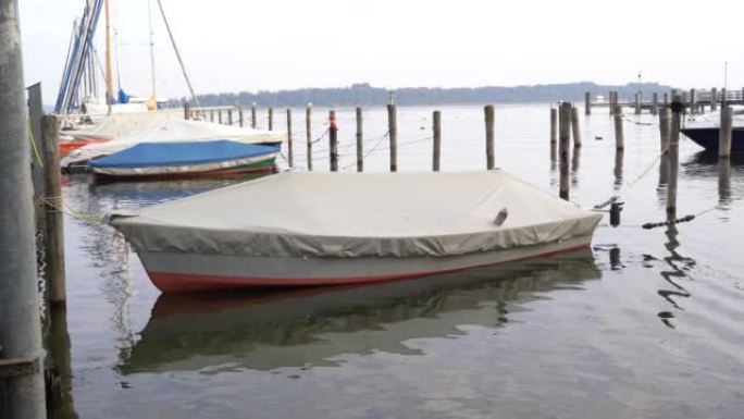 一艘被覆盖并绑在木柱上的船早上漂浮在湖中