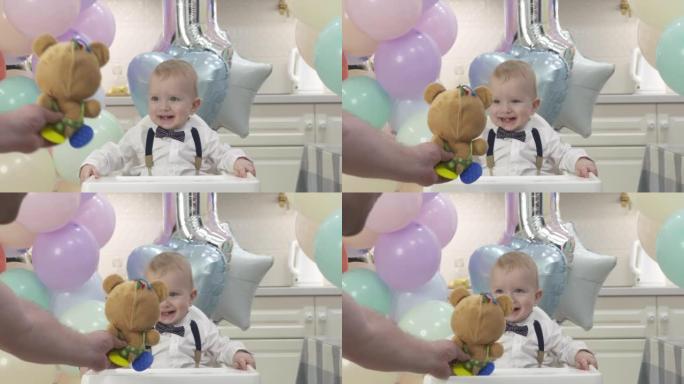 父亲在生日聚会上给快乐的孩子一个玩具，一岁的男婴庆祝他的第一个生日，可爱的孩子在家里对着五颜六色的气