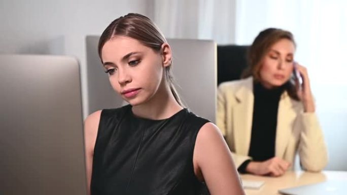两名年轻的成年妇女在办公室或计算机上的办公空间工作。两名休闲女商人在现代办公场所工作