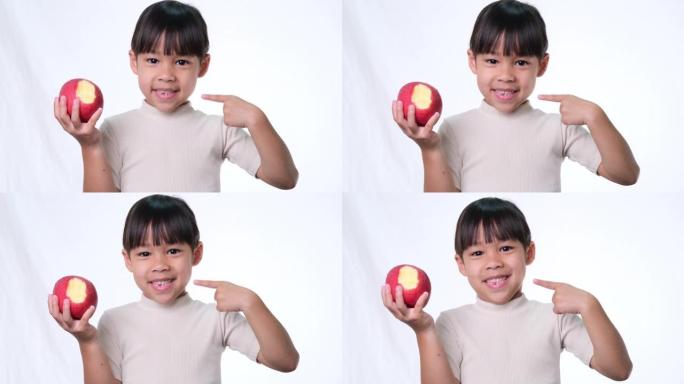 快乐的苹果小女孩。可爱的亚洲小女孩在工作室吃白色背景的有机苹果。儿童健康营养。