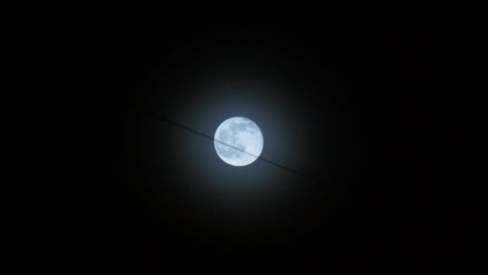 在夜黑的天空的背景下，满月是蓝色的，这是建筑物上悬挂的电线