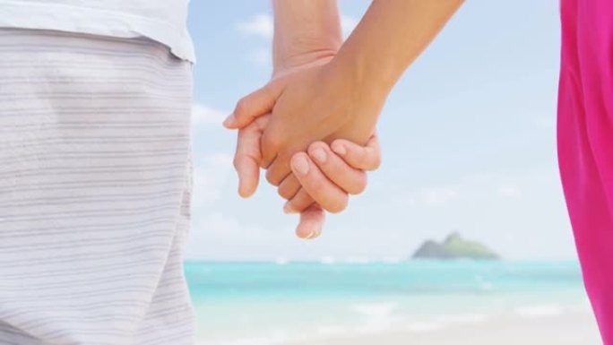 恋爱中的海滩情侣牵手度蜜月。粉色连衣裙，休闲沙滩装浪漫的新婚夫妇站在旅行暑假。